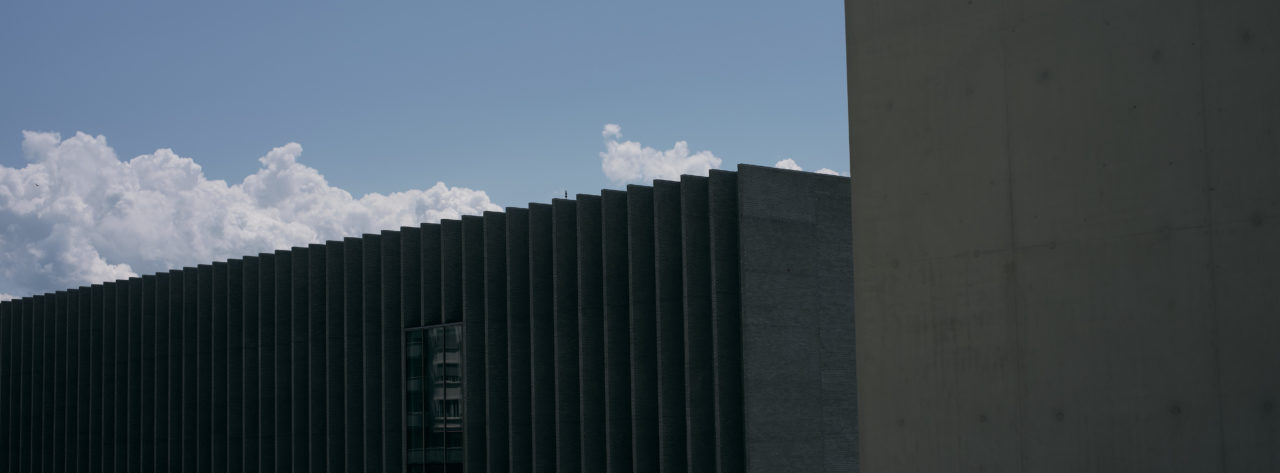 Photographie de l'extérieur d'un bâtiment de la plateforme 10. Style cinématique avec des couleurs froides et motifs géométriques.